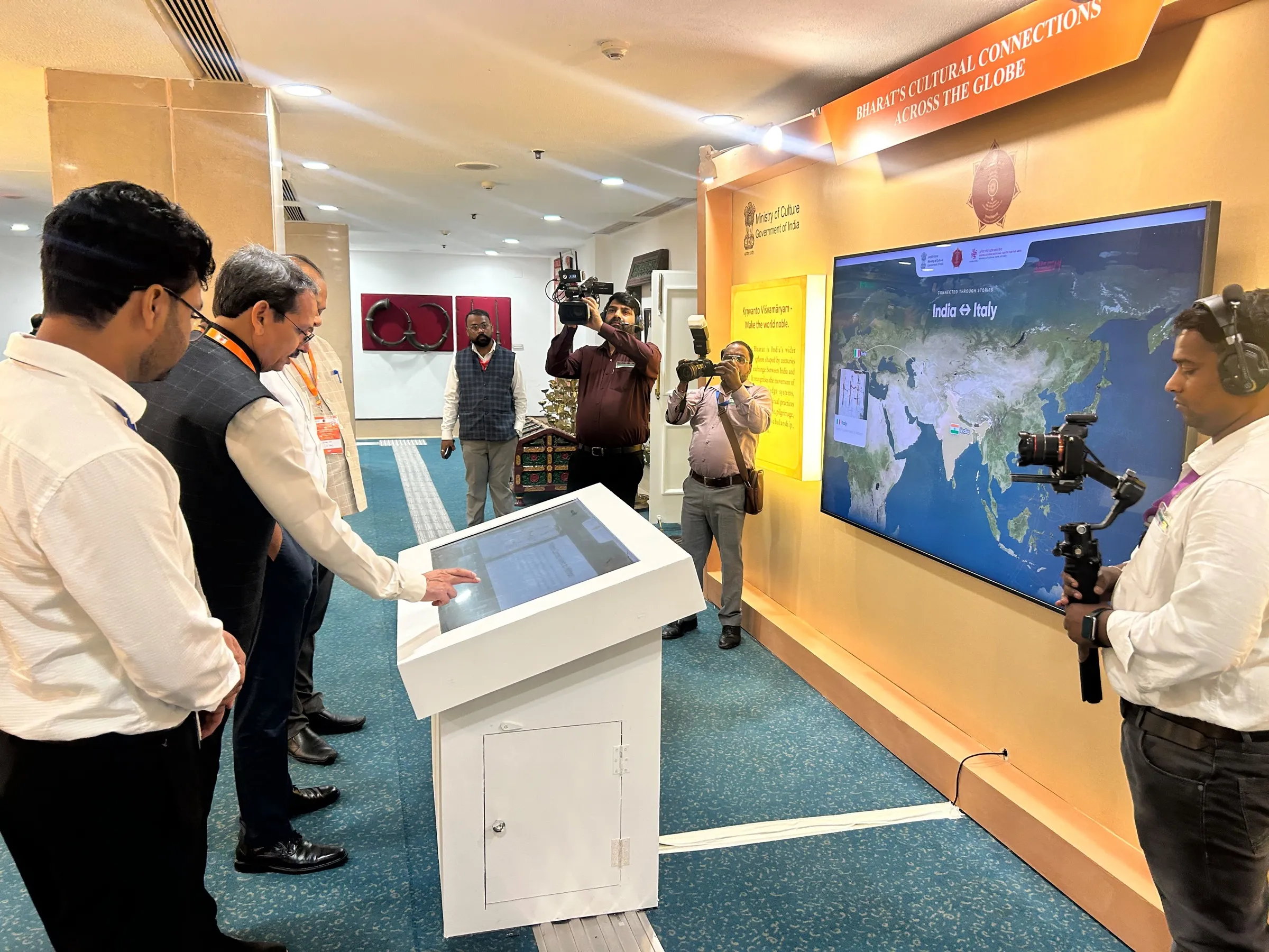An official uses the kiosk while camera operators with a gimbal and stills cameras film.